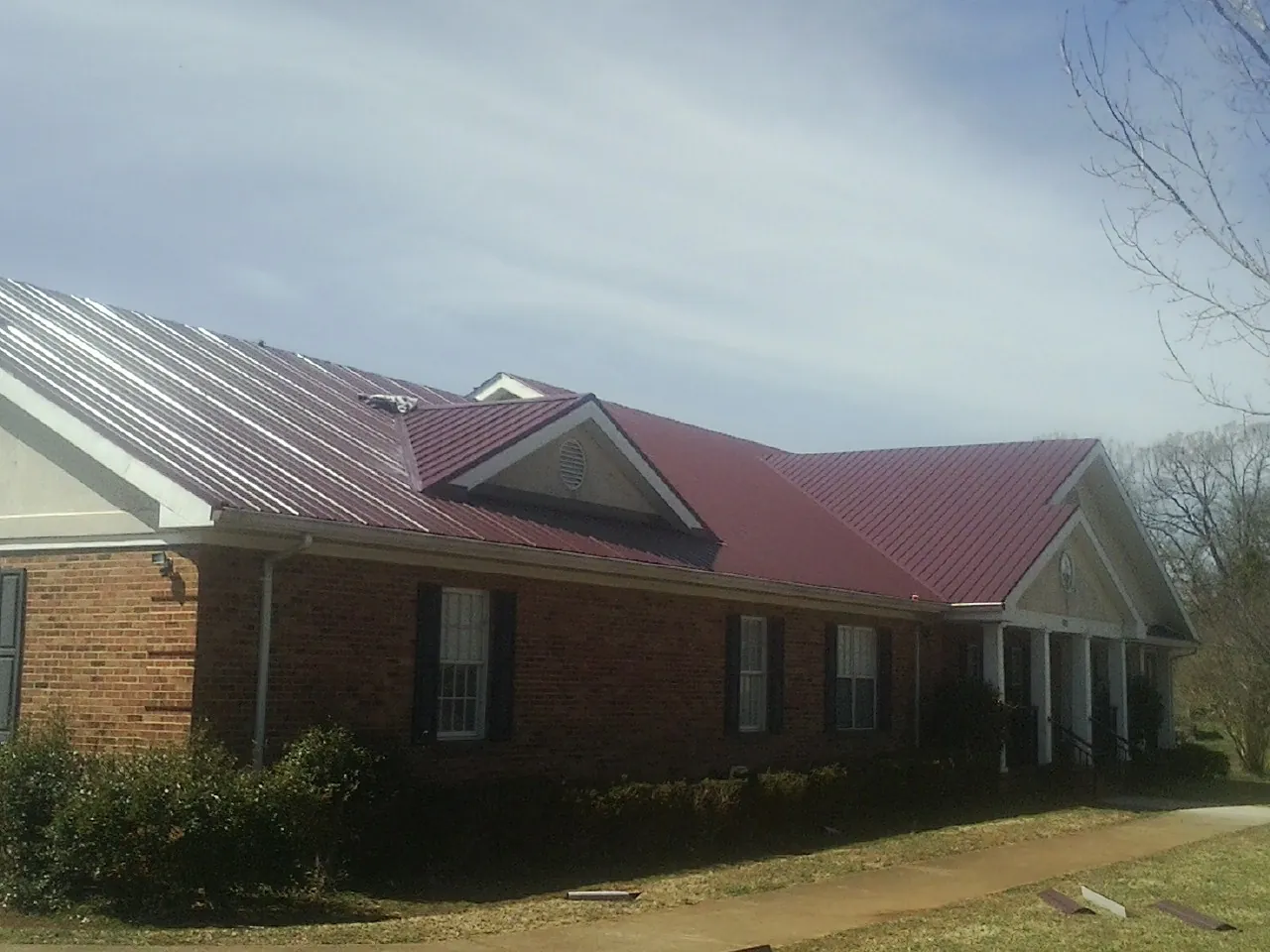 Red metal roof with gabled entries on a long brick building, from a Hail Damage Roof Repair job in Sparrows Point