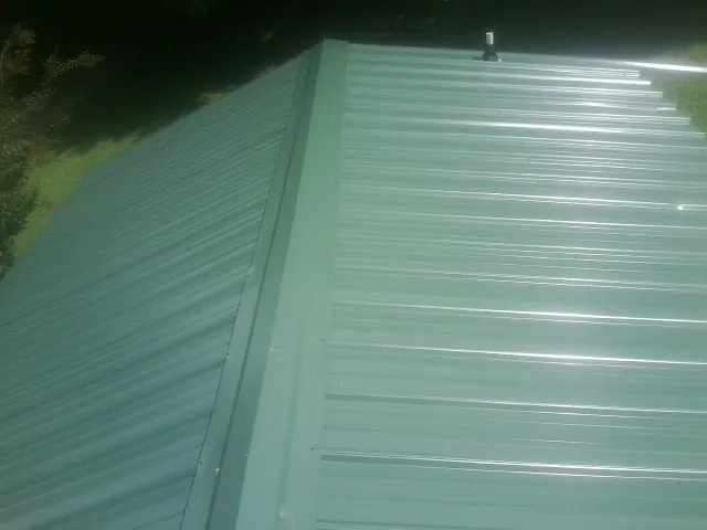 New green metal panels meeting at the ridge of a roof — Flat Roof Repair work by our crew in Sparrows Point
