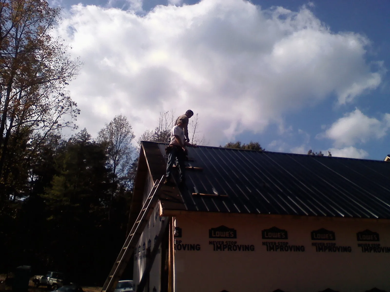 Roofer fastening dark metal panels high against a cloudy sky, from a Roof Inspection job in Sparrows Point