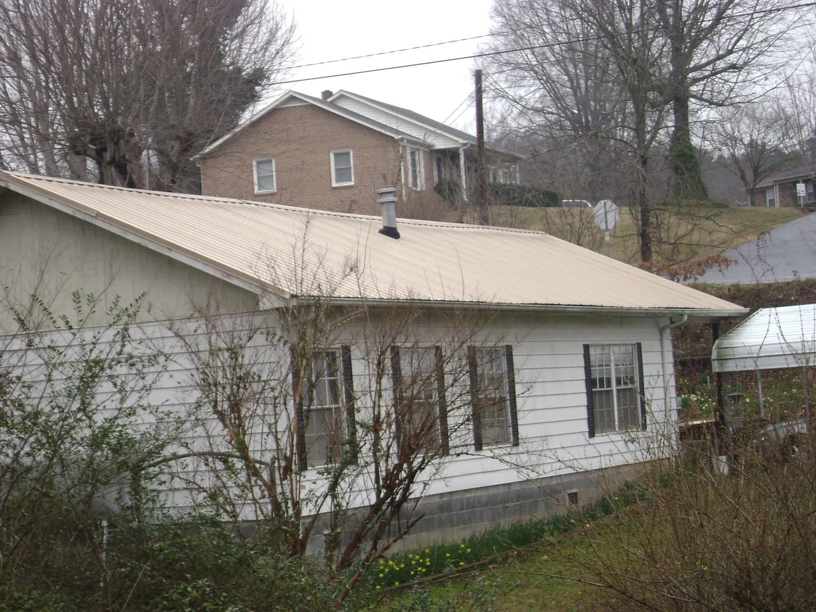 Tan metal roof on a white sided house set into a hillside — Commercial Roofing by Roofing Brothers in Sparrows Point